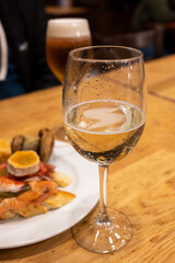 Board with typical snacks of Basque Country, pinchos or pinxtos, skewers or small piece of bread with toppings, served with glass of txakoli wine in bar in San-Sebastian or Bilbao, Spain