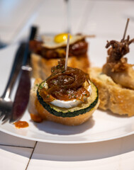 White board with typical snack of Basque Country, pinchos or pinxtos skewers with small pieces of bread, courgette, sea food, eggs, cheese, served in bar in San-Sebastian or Bilbao