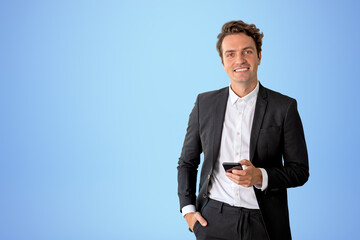 Businessman with smartphone in hand, happy portrait on empty blue background