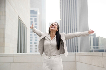 Victorious hispanic business woman raising her arms up to the sky, celebrating her success and achievements for her new career - 557612830