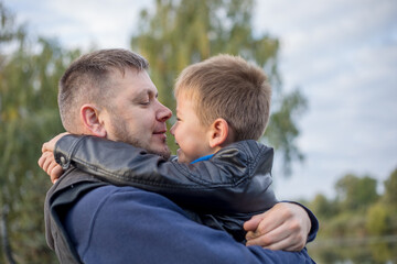 Happy father and son hugging and playing together in green nature. Fisherman's house with a wooden pedestrian bridge on a tiny island in the middle of the lake.