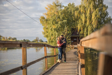 Happy young couple in love walking in bridge at sunset. Man embracing and going to kiss sensual woman.