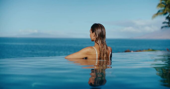 Woman relaxing in luxury infinity pool looking out at the ocean, tropical resort spa vacation