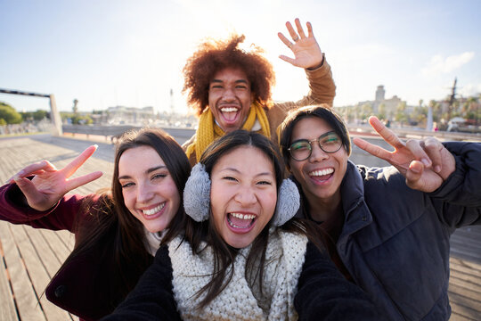 Selfie of a group of happy people taking selfie photo looking at the camera with a mobile phone in winter clothes. Young smiling mixed race friends having fun in a cold and sunny day.