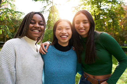 Portrait of three girls outside looking at the camera. An Asian Chinese woman, a black African American and a Caucasian lady together and embracing. Friendship in multi-ethnic groups of people
