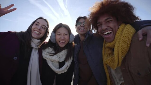 Selfie of a group of happy people taking selfie photo looking at the camera with a mobile phone in winter clothes. Young smiling mixed race friends having fun in a cold and sunny day.