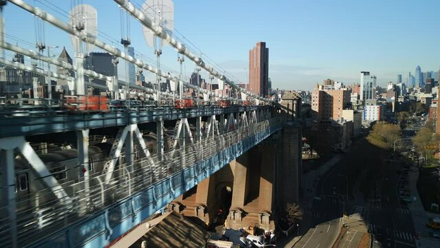 Forwards fly along double decked Manhattan Bridge. Tracking of subway train. High rise buildings in urban borough in background. New York City, USA