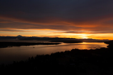 Sunrise Aerial View of Lummi Island and the Mainland With a Ferryboat Making a Morning Crossing. Just before the sun rises over the Cascade Mountains dramatic clouds form in the east and south. 