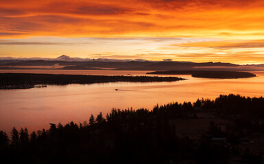 Sunrise Aerial View of Lummi Island and the Mainland With a Ferryboat Making a Morning Crossing. Just before the sun rises over the Cascade Mountains dramatic clouds form in the east and south. 