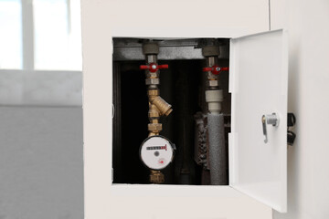 Water meter hidden in niche on white wall indoors