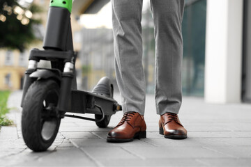 Businessman with modern kick scooter on city street, closeup © New Africa