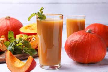 Tasty pumpkin juice and pumpkins on white wooden table