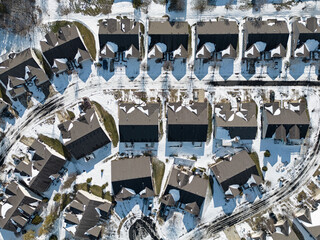 Modern duplex (aka two-family dwelling) houses in a neighborhood are shown from above during a winter day, with snow mostly covering the roads and ground.