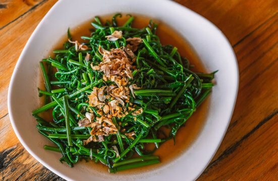 Stir-fried Phak Kut or Paco fern with garlic and oyster sauce. The healthy vegetable food menu of Thailand's traditional food, top view image food on white plate on wooden table.