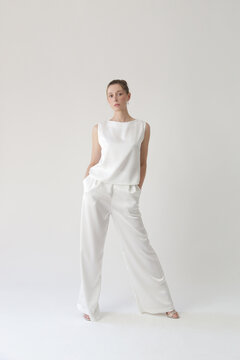 Serie of studio photos of young female model in all white silk outfit, sleeveless blouse and wide legs trousers