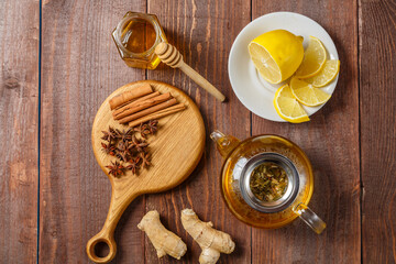 On the table on a wooden board anise, cinnamon, ginger and honey and a teapot with tea top view.