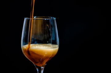 Pouring dark beer into a glass isolated on a black background.
