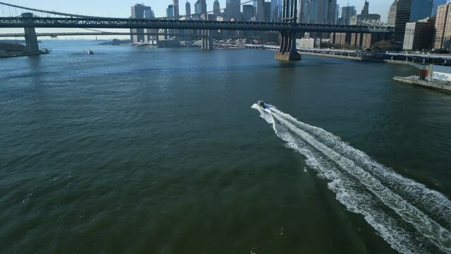 Aerial view of small motorboat moving on wide river in metropolis. White trail on water surface after vessel. New York City, USA