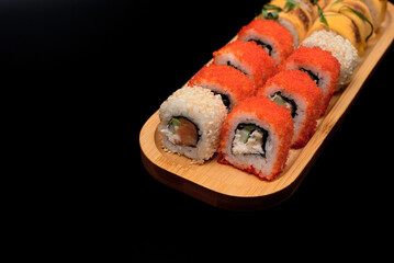 Delicious Japanese rolls with salmon, avocado, cucumber, cheese on wooden plate with selective focus on black background. Asian food concept. Healthy eating