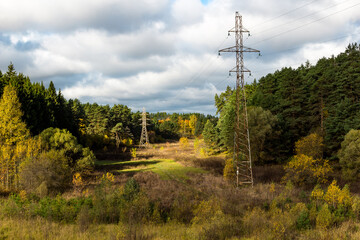 Obraz premium High-voltage power line passing through a picturesque valley surrounded by autumn nature, electric wires suspended on high metal poles