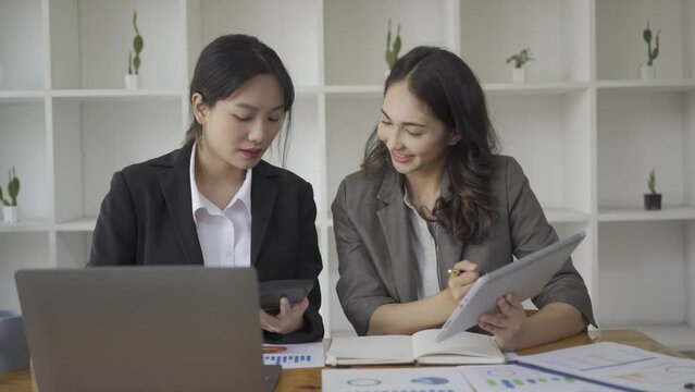 Two asian businesswoman analyzing chart data in document Use files and documents to create with a laptop with Colleagues Working in the Office 4K