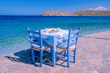 Crete Greece Plaka Lassithi with its traditional blue table and chairs and the beach in Crete Greece. Paralia Plakas, Plaka village Crete - obrazy, fototapety, plakaty