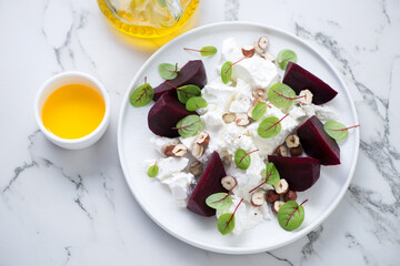 Plate with beetroot, feta cheese and nuts salad on a white marble background, high angle view,...