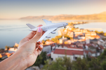Naklejka premium Hand with toy airplane. Air transport ticket prices and travel concept. Resort sea town in the background