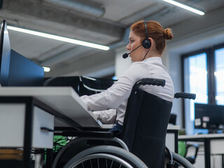 Red-haired caucasian woman in a wheelchair talking on a headset. Female call center worker at her...