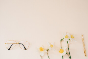 Bouquet of spring flowers daffodils and women's glasses on a beige desktop with a copy space