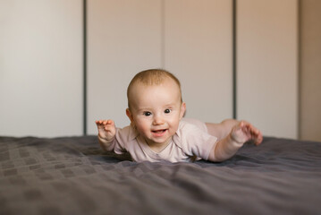 Fototapeta premium Cute smiling baby boy in bed lying on his belly in bedroom
