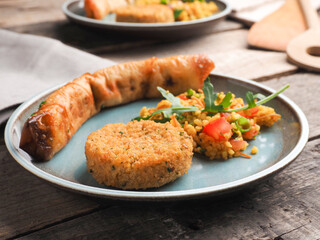 Tasty falafel with spicy bulgur and a vegetarian dough roll on a wooden table