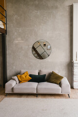 Stylish modern grey sofa with pillows in the living room with grey walls and a round mirror in Scandinavian style