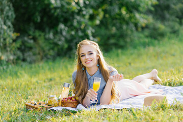 Pretty caucasian young woman with long hair is lying on a blanket in nature on a sunny summer day. Picnic, rest, relax in the fresh air.