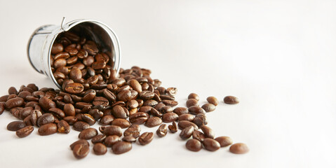 A metal bucket with a pile of scattered roasted coffee beans.