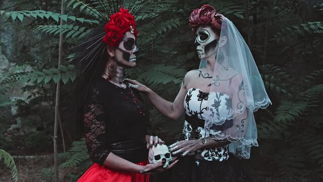 Two Young Women with a design on the face and neck in the style of the Goddess of Death or Katarina conjure over a sugar skull holding it in their hands. Close-up on hands. Festival Day of the Dead