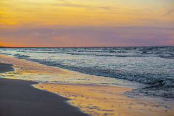 Fototapeta na wymiar Photo of pink and yellow sunset over sea and small waves close up and reflection of the sky in the wet sand - Jurmala, Latvia