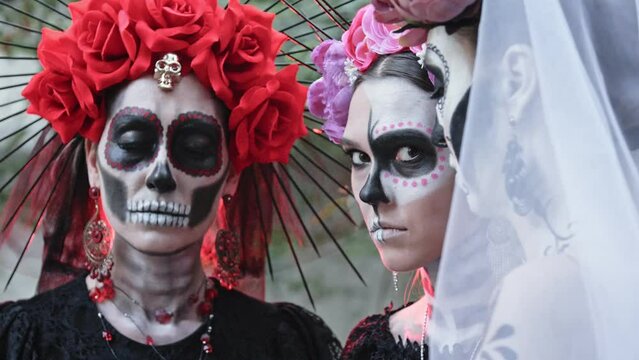 Three Young Women with a design on the face and neck in the style of the Goddess of Death or Katarina conjure over a sugar skull while holding it in their hands. Close-up on the eyes