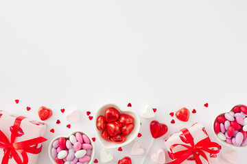 Valentines Day concept. Flat lay photo of red gift boxes, heart shaped saucers with sweets candies and lollipops, heart marshmallow on white background with copy space. Sweet Valentines card idea.