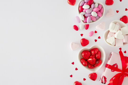 St Valentines Day concept. Flat lay photo of red gift boxes, heart shaped saucers with sweets candies and lollipops, heart marshmallow on white background with copy space. Sweet Valentines card idea.