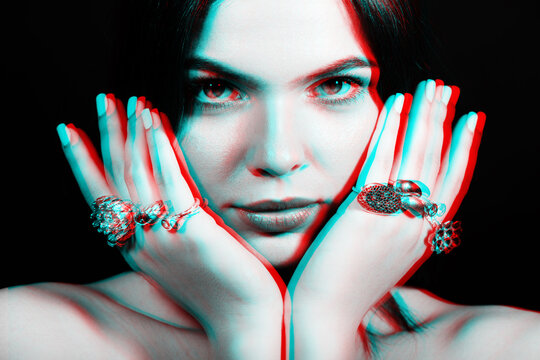 Studio portrait of beautiful woman with fancy various rings on her fingers in red and blue color split effect. Model holding hands near her face and looking at camera. Futuristic looking style