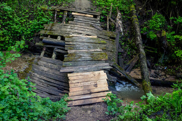 Old broken wooden bridge over a ravine with a stream
