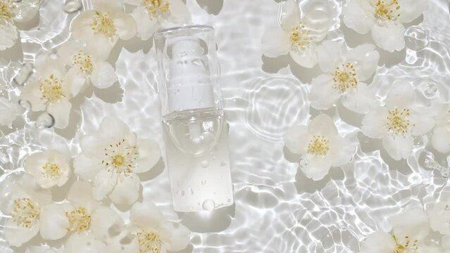 Cosmetic bottle, vial and jasmine petals flowers on water surface with drops. Pure water with reflections sunlight and shadows. Slow motion of waves water. Design, advertising, products. 4k