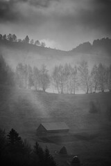 Ray of light in a misty autumn countryside landscape. Small hut and haystack. Black and white
