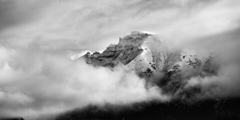 Black and white panoramic alpine landscape of mountain top covered by snow and clouds