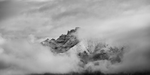 Black and white panoramic landscape of mountain top covered by snow and clouds