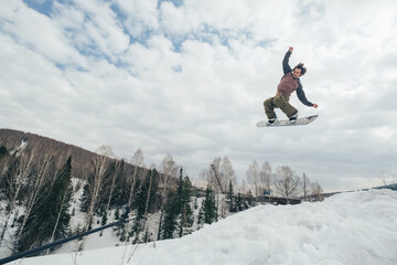 Naklejka na ściany i meble Snowboarder flying jumping from kicker in winter cloudy day