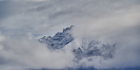 Panoramic landscape image of mountain top covered by snow and clouds