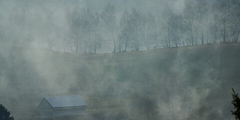 Misty autumn countryside landscape with a small hut 
