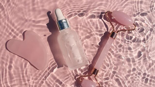Cosmetic bottle with pipette and Massage roller on water with drops on a pink background. Pure water with reflections sunlight and shadows. Video of packaging for advertising, products High quality 4K